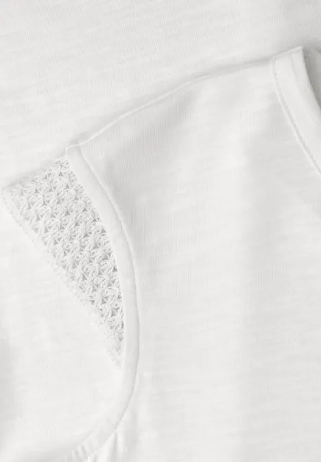 Close-up van een wit t-shirt met fijn kant bij de mouw en subtiele stofstructuur.