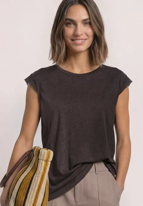 Shirt met afhangende schouders en gehaakte details black coffee Lachende vrouw met donkerbruin shirt en beige broek, met een gestreepte tas in geel, wit en bruintinten.
