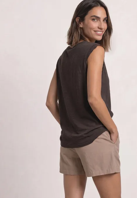Shirt met afhangende schouders en gehaakte details black coffee Vrouw in zwart mouwloos topje en beige short, staand opzij, hand in zak, glimlachend over haar schouder kijkend.