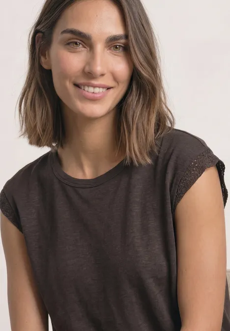 Shirt met afhangende schouders en gehaakte details black coffee Portret van een glimlachende jonge vrouw met bruin haar en donkerbruin T-shirt op een lichte achtergrond.