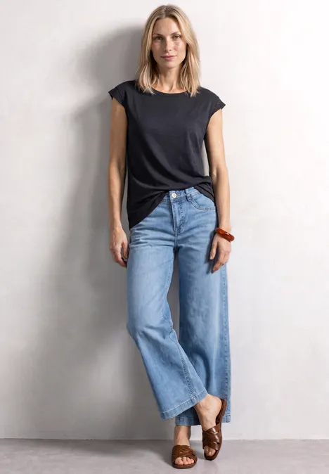 Vrouw in zwart t-shirt en wijde jeans voor een witte muur.