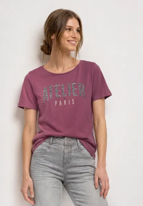 Shirt met ronde hals en opdruk op de voorkant dark clouded blush Vrouw in een roze 'Atelier Paris'-shirt en grijze jeans tegen een neutrale achtergrond.