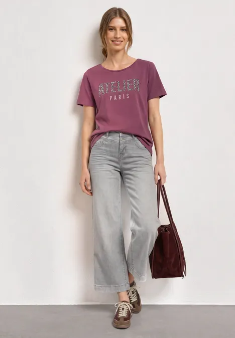 Shirt met ronde hals en opdruk op de voorkant dark clouded blush Vrouw in casual outfit: paars T-shirt, wijde jeans, sneakers en een grote bordeaux tas.