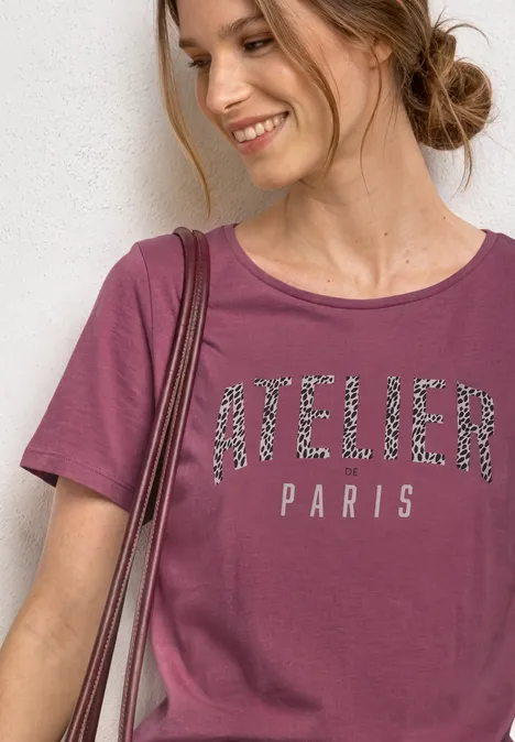 Shirt met ronde hals en opdruk op de voorkant dark clouded blush Glimlachende vrouw in bordeaux t-shirt met 'ATELIER PARIS', zijknot, voor een lichte muur.