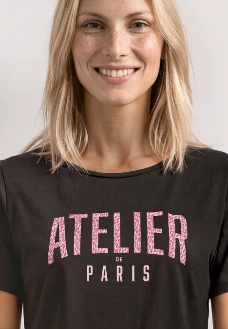 Femme aux cheveux blonds porte un T-shirt noir avec l’inscription « ATELIER Paris ».