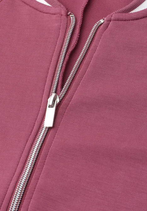 Nahaufnahme eines Reißverschlusses an einem rosa bis burgunderfarbenen Kleidungsstück.