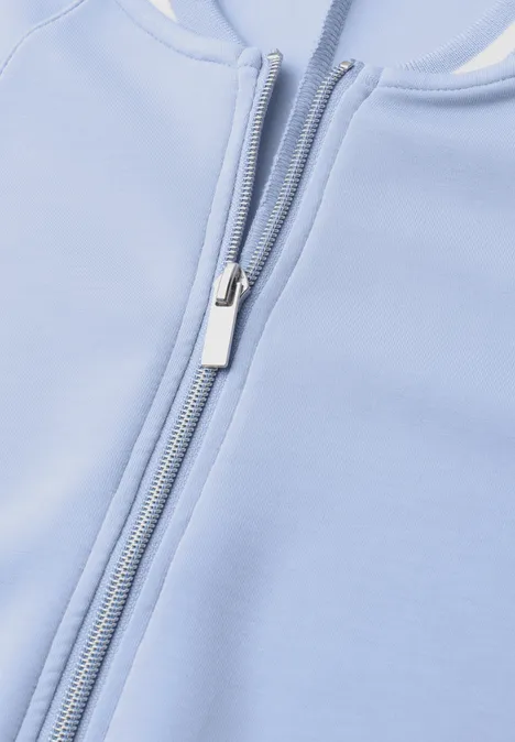 Close-up van een lichtblauw kledingstuk met een zilverkleurige rits.
