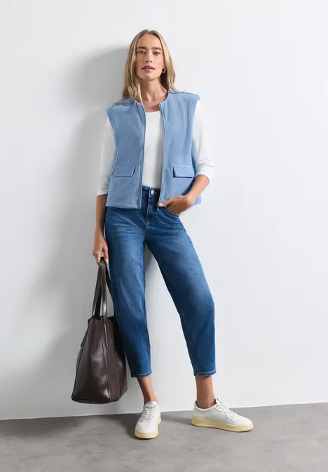 Gilet zippé à col rond effet velours côtelé northern blue Femme en chemise blanche, gilet bleu clair, jean bleu, baskets blanches et sac à main marron.