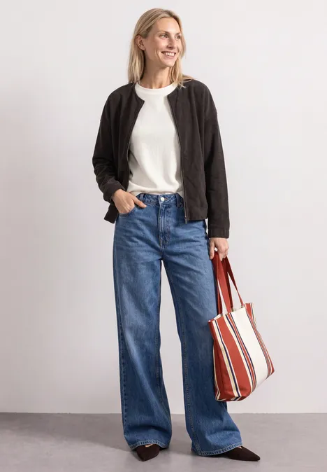 Jasje met ronde hals in corduroy-look black coffee Frau in schwarzer Jacke, weißem Shirt, weitem Jeans und gestreifter Umhängetasche.