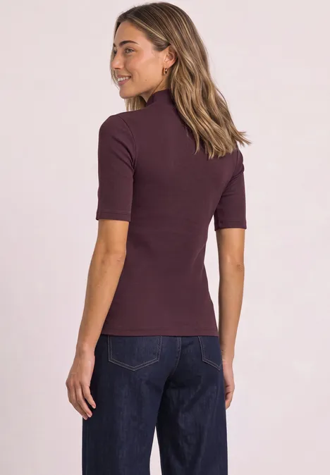 T-shirt à col roulé en maille côtelée rustic rouge Frau von hinten, trägt ein bordeauxfarbenes Kurzarmshirt und dunkle Jeans.