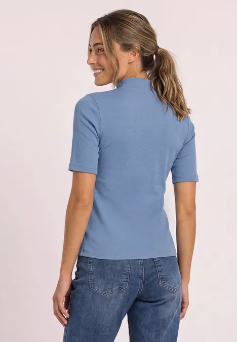 Shirt met col in ribbelpatroon northern blue Junge Frau von hinten, trägt hellblaues Shirt und Jeans, schaut lächelnd über die Schulter.