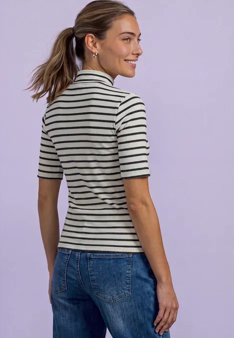 Femme de dos en T-shirt rayé et jean, souriante, cheveux attachés, fond violet clair.