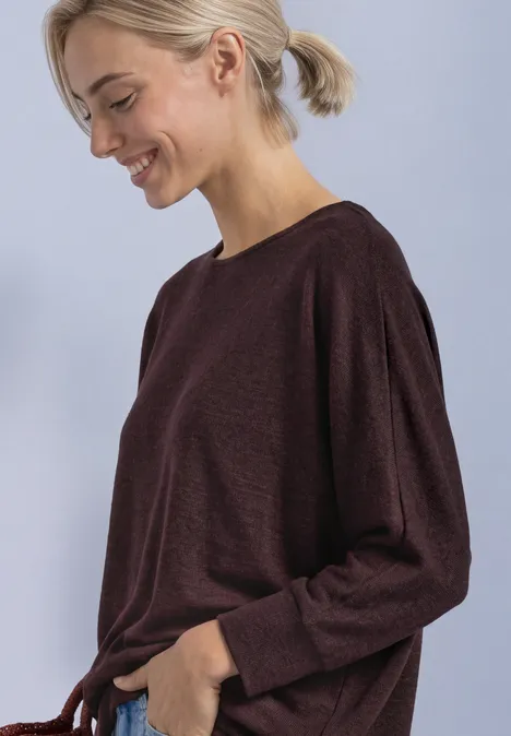 Frau mit hellem Pferdeschwanz trägt ein langärmeliges, burgunderfarbenes Shirt und lächelt im Profil.