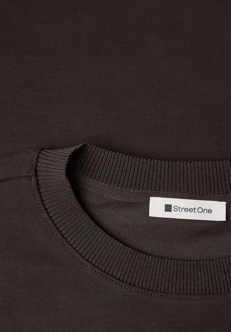 Close-up van een zwart T-shirt met ronde hals en een 'Street One'-label in de nek.