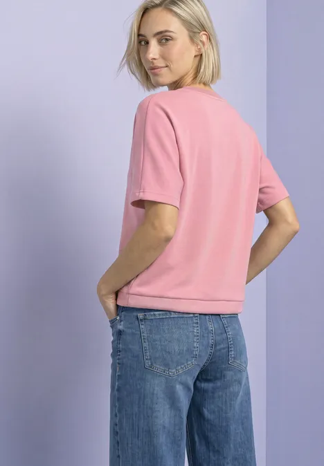 T-shirt à col rond aspect soyeux vintage blush Jeune femme portant un T-shirt rose et un jean bleu, vue de côté.