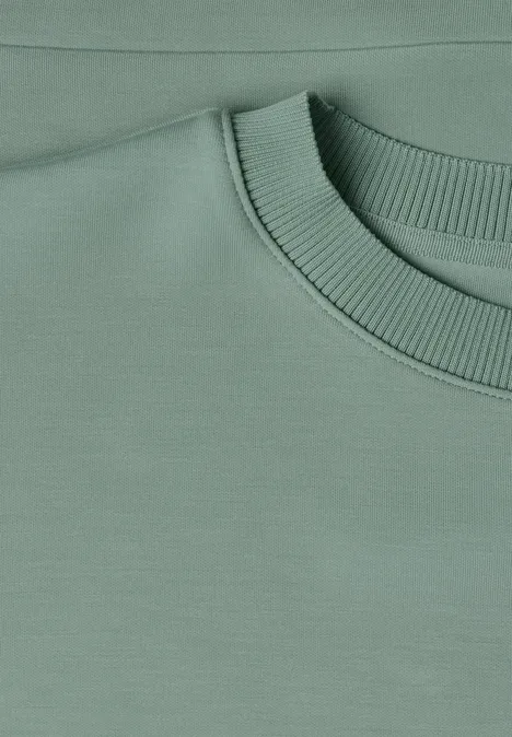 Close-up van een pastelgroene sweater met geribbelde ronde hals.