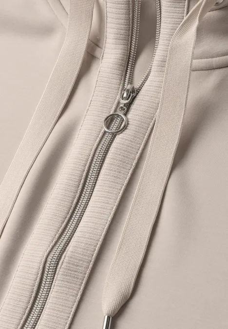 Gros plan d’un sweat à capuche beige avec fermeture éclair et cordons.