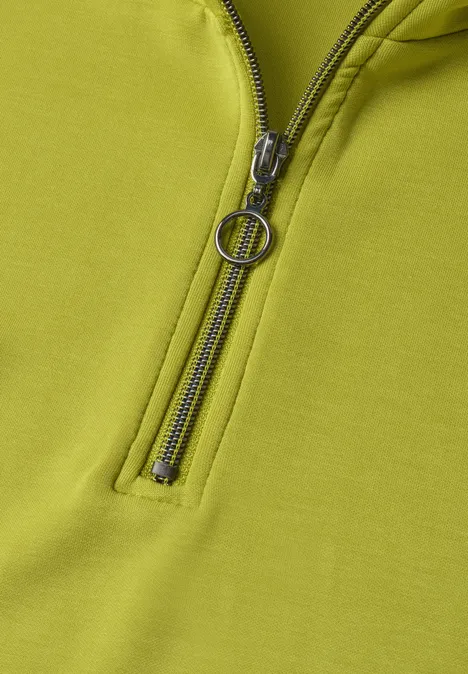 Nahansicht eines hellgrünen Oberteils mit Reißverschluss und rundem Zipper-Anhänger.