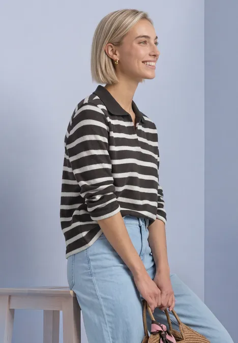 3/4-Arm Poloshirt mit Streifenmuster black coffee Eine lächelnde Frau mit kurzem blondem Haar, gestreiftem Pullover und hellblauer Jeans lehnt sich seitlich ab.