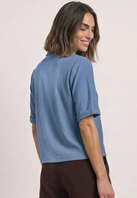 Chemise aux textures variées et à boutons northern blue Frau in blauem Kurzarmhemd und brauner Hose, seitlich gewandt und lächelnd