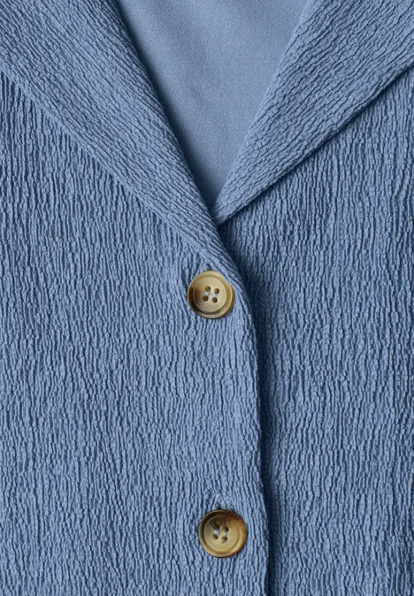 Chemise aux textures variées et à boutons northern blue Makroaufnahme einer blau strukturierten Jacke mit zwei runden Holzknöpfen.