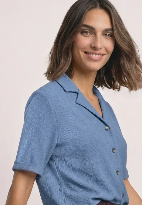 Chemise aux textures variées et à boutons northern blue Frau mit braunen Haaren in blauem Kurzarmhemd, die lächelnd in die Kamera blickt.