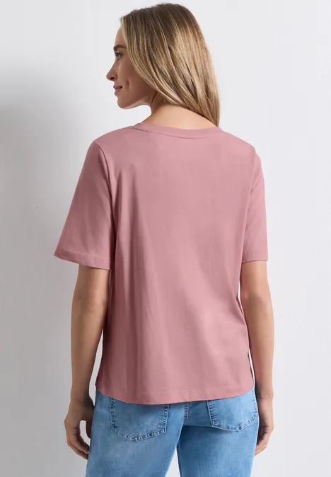 Shirt met ronde hals en fotoprint vintage blush Frau von hinten in rosa T-Shirt und blauen Jeans vor hellem Hintergrund.