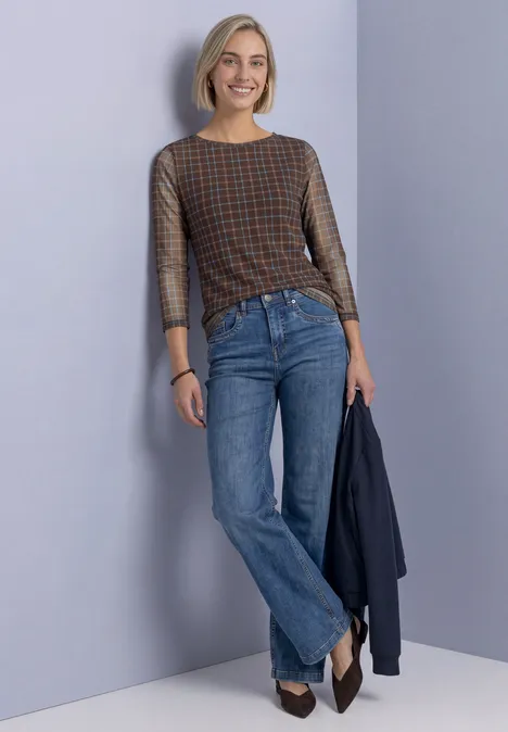 3/4-Arm Shirt aus Mesh mit Print silk brown Frau mit kurzem blonden Haar, kariertem Oberteil und blauen Jeans lehnt an Wand und hält eine Jacke.