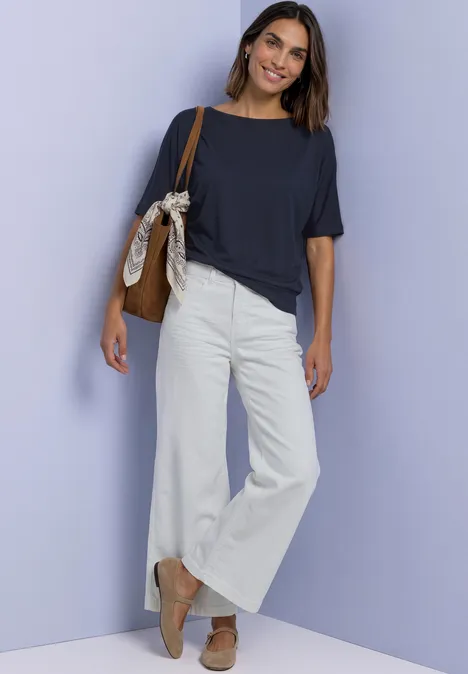 Frau trägt weites weißes Bündchenhose, dunkles T-Shirt, Halbschuhe, Tasche an der Schulter