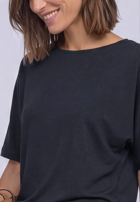 Eine lächelnde Frau mit schulterlangen braunen Haaren trägt ein schlichtes schwarzes T-Shirt.