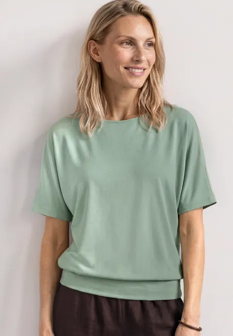 Basic Shirt met boothals en elastische zoom eucalyptus green Vrouw in mintgroen T-shirt en donkere broek tegen lichte achtergrond.