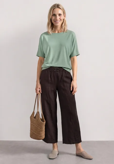 Basic Shirt met boothals en elastische zoom eucalyptus green Vrouw draagt mintgroen T-shirt, zwarte wijdvallende broek, strooien draagtas en comfortabele platte schoenen.