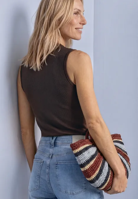 Aspect soyeux à col roulé black coffee Frau von der Seite in Jeans und schwarzem Top, hält bunte gestreifte Tasche.