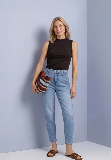 Aspect soyeux à col roulé black coffee Frau mit schwarzem Top und hellblauen Jeans, trägt gestreifte Tasche und braune Sandalen.