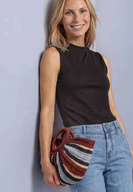 Aspect soyeux à col roulé black coffee Lächelnde Frau in schwarzem Top und Jeans hält eine bunte, gestreifte Flechttasche.