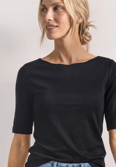 Gros plan d'une femme souriante aux cheveux blonds attachés portant un t-shirt noir.