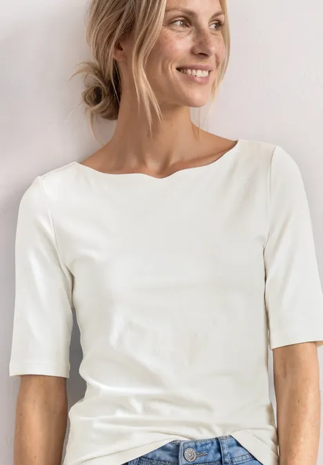 Shirt met golvende halslijn in effen kleur off white Persoon draagt een wit shirt met driekwart mouwen tegen een lichte achtergrond.