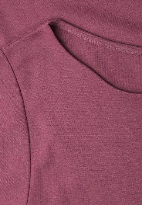 La photo montre un T-shirt bordeaux en gros plan, col rond et couture apparente.