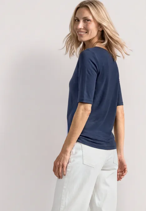 Femme de dos en t-shirt bleu marine et pantalon blanc sur fond neutre