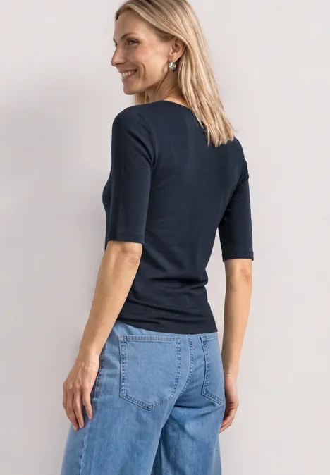 Une femme vue de dos portant un t-shirt bleu marine à manches courtes et un jean bleu clair.