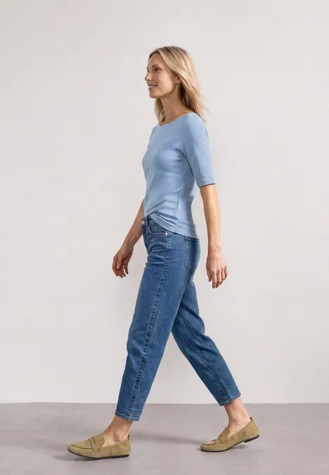 T-shirt à encolure ondulée, couleur unie northern blue Frau in blauem Shirt und Jeans läuft seitlich vor hellem Hintergrund.