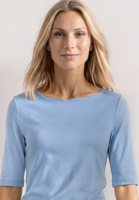T-shirt à encolure ondulée, couleur unie northern blue Frau in hellblauem Halbarmshirt vor neutralem Hintergrund