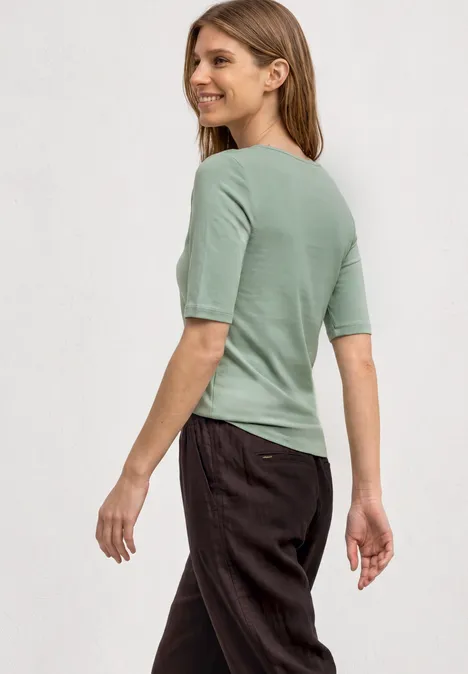 Eine Frau von hinten in einem pastellgrünen Kurzarmshirt und dunklen Hosen.