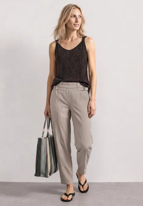 Top met V-hals en decoratief detail molten earth Frau trägt schwarzes Top, helle Hose, Flip-Flops und Tasche, lässiger Sommerlook.