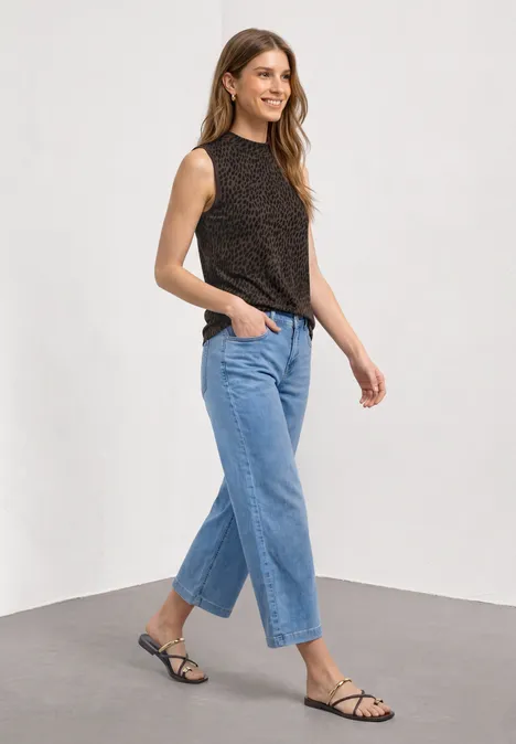 Top mit Turtle Neck und Print molten earth Eine Frau in einem ärmellosen, schwarz gemusterten Top, blauen Jeans und flachen, schwarzen Sandalen.