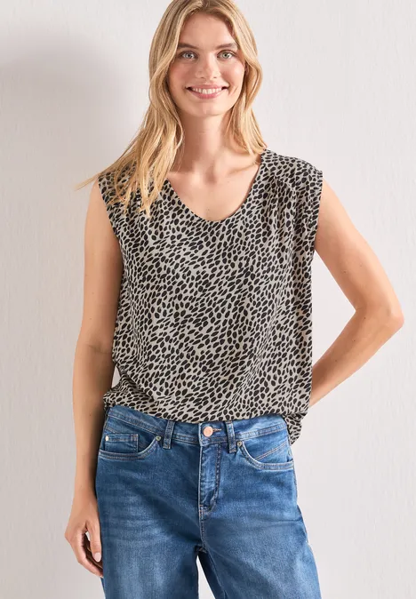 Frau trägt ärmelloses Leoprint-Top und blaue Jeans vor neutralem Hintergrund.