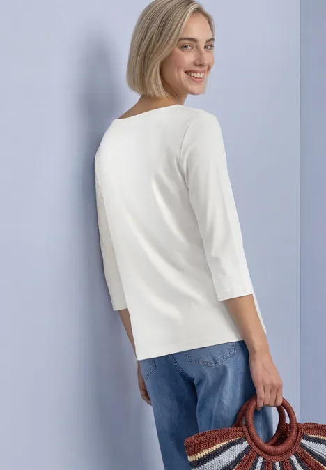 3/4-Arm Shirt mit U-Boot-Ausschnitt off white Frau im Profil, Blick über die Schulter, trägt ein weißes 3/4-Arm-Shirt, blaue Jeans und eine runde Flechttasche.