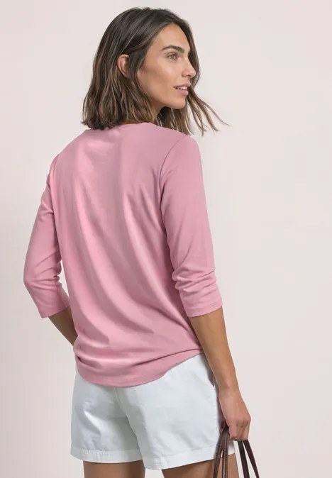 3/4-Arm Shirt mit U-Boot-Ausschnitt vintage blush Frau von hinten in rosa Langarmshirt und weißen Shorts, hält eine Tasche und blickt seitlich.