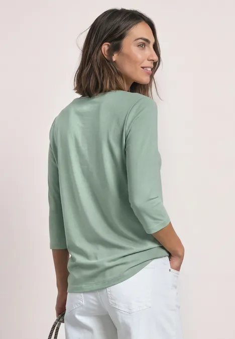 3/4-Arm Shirt mit U-Boot-Ausschnitt eucalyptus green Frau von hinten in mintgrünem Shirt mit 3/4-Ärmeln und weißen Hosen vor neutralem Hintergrund.