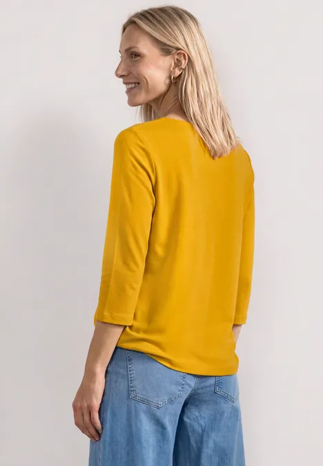 3/4-Arm Shirt mit U-Boot-Ausschnitt saffron yellow Eine Frau von hinten in senfgelbem Oberteil mit 3/4-Ärmeln und blauer Jeans.